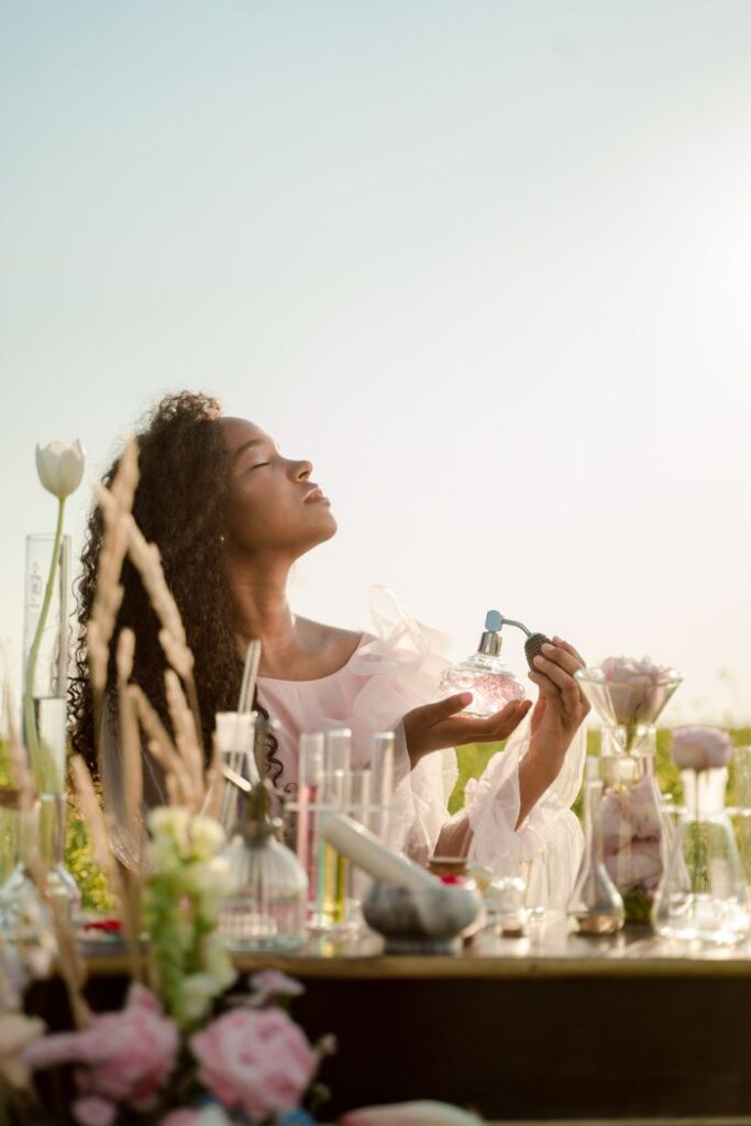 Woman enjoying fragrance creation outdoors amidst glassware and nature.