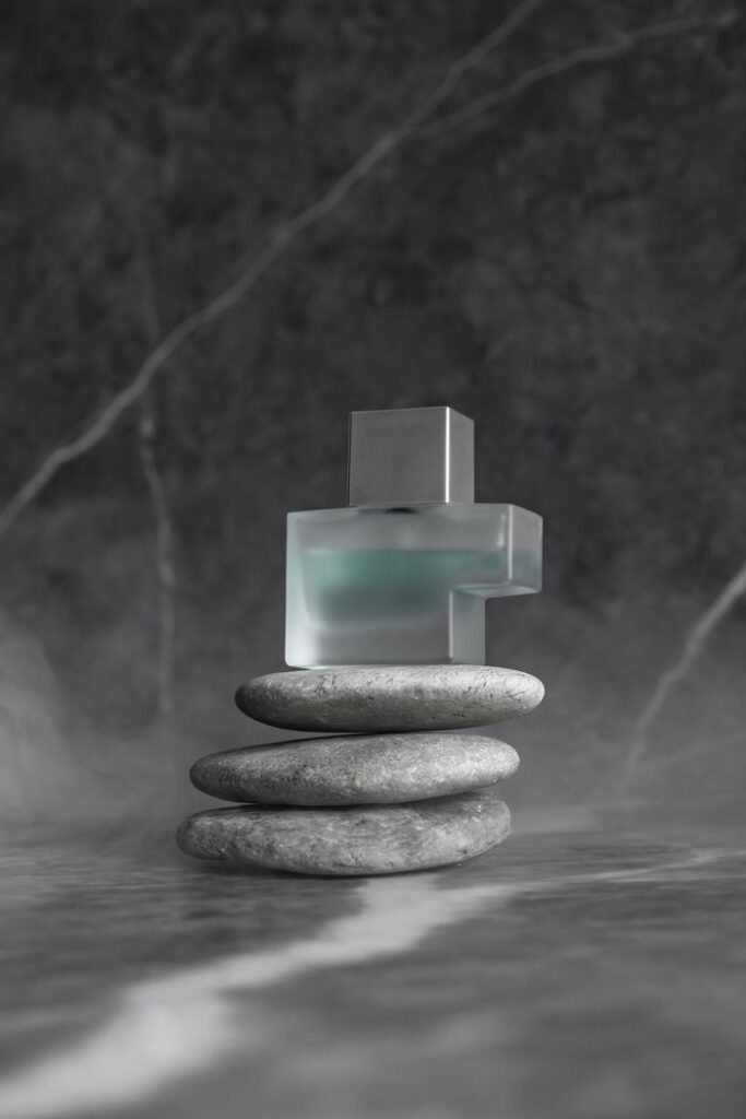 A sleek perfume bottle elegantly placed on stacked stones with a gray background.