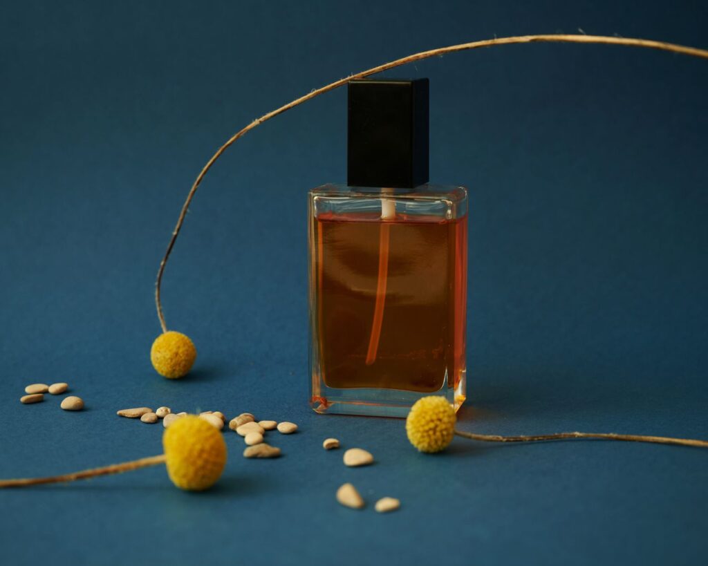 Elegant perfume bottle with yellow flowers and seeds on a blue background. Perfect for product mockups.