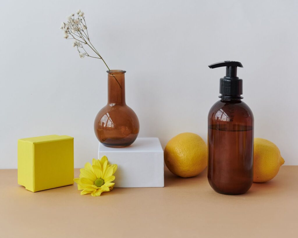 Artistic still life featuring a brown glass bottle, lemons, and a flower on a neutral background.